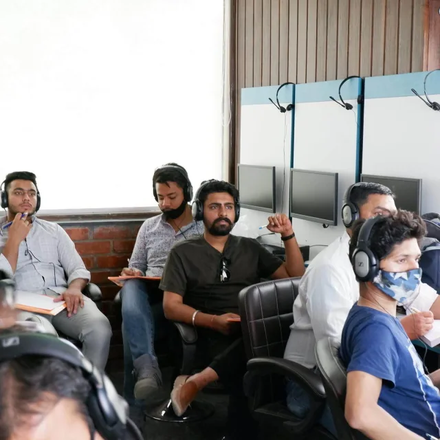 Students wearing over-ear headsets and making notes on paper during a listening practice session.