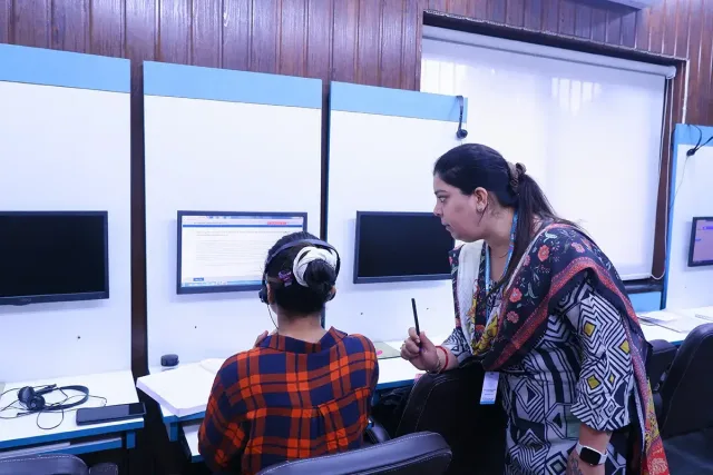 A trainer leaning over a student's shoulder to talk through what is on the screen in front of them.