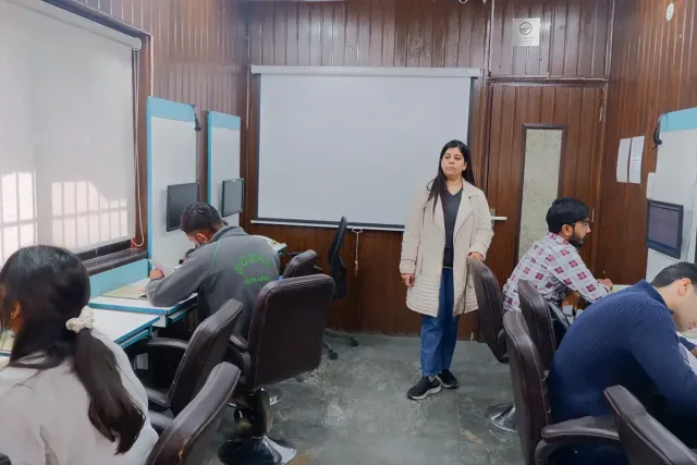 A trainer standing between the workstations while students work at their screens.
