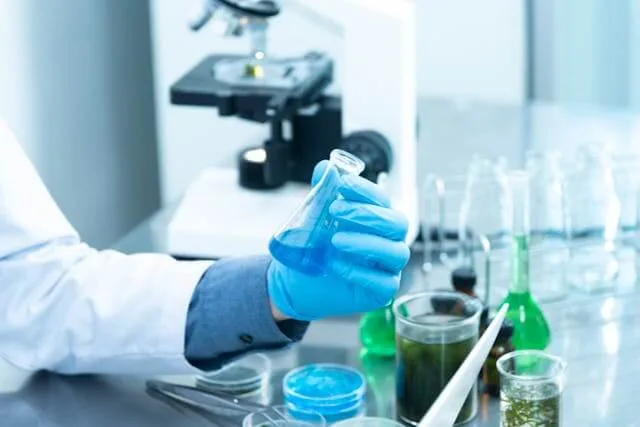 A researcher holding a flask beside a microscope in a laboratory