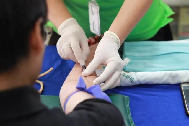 A gloved clinician taking a blood sample from a patient’s arm