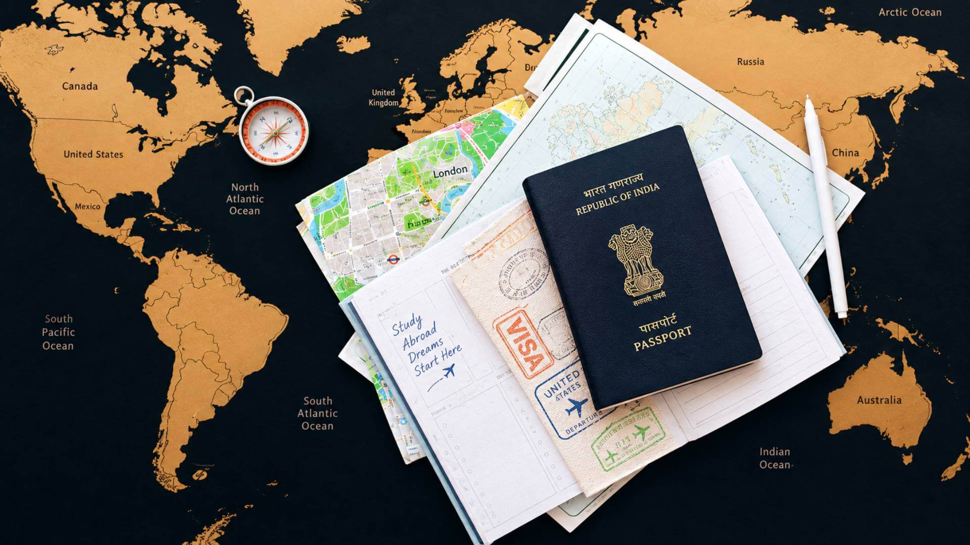 An Indian passport, visa stamps, travel maps and a compass laid out on a world map, beside a notebook reading "Study Abroad Dreams Start Here"