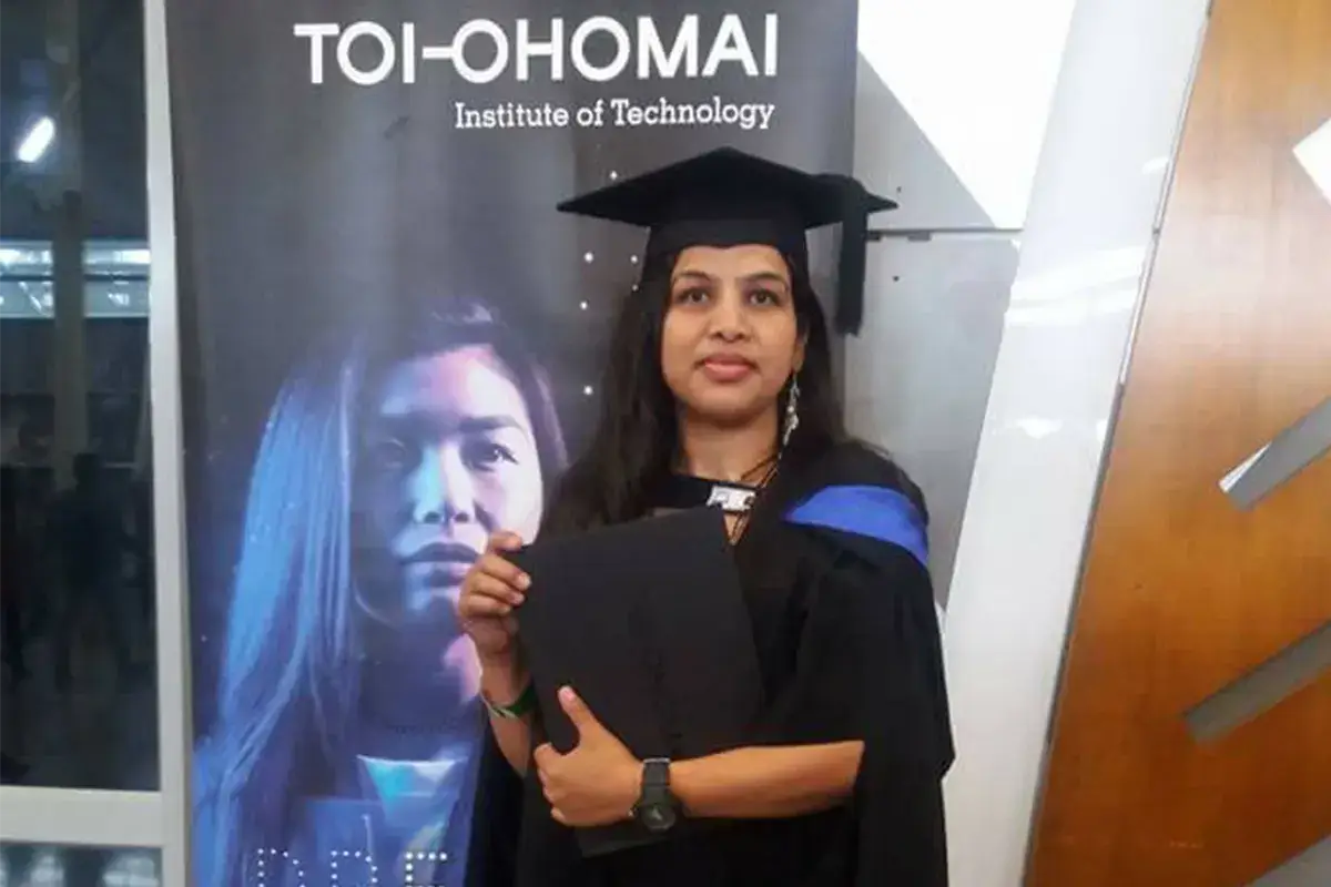 A graduate in cap and gown holding her degree folder at her graduation ceremony